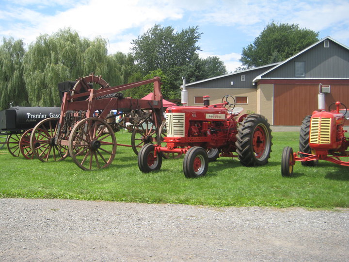 Exterior photo of the red brick museum in the background and old farming equipment in the foreground.